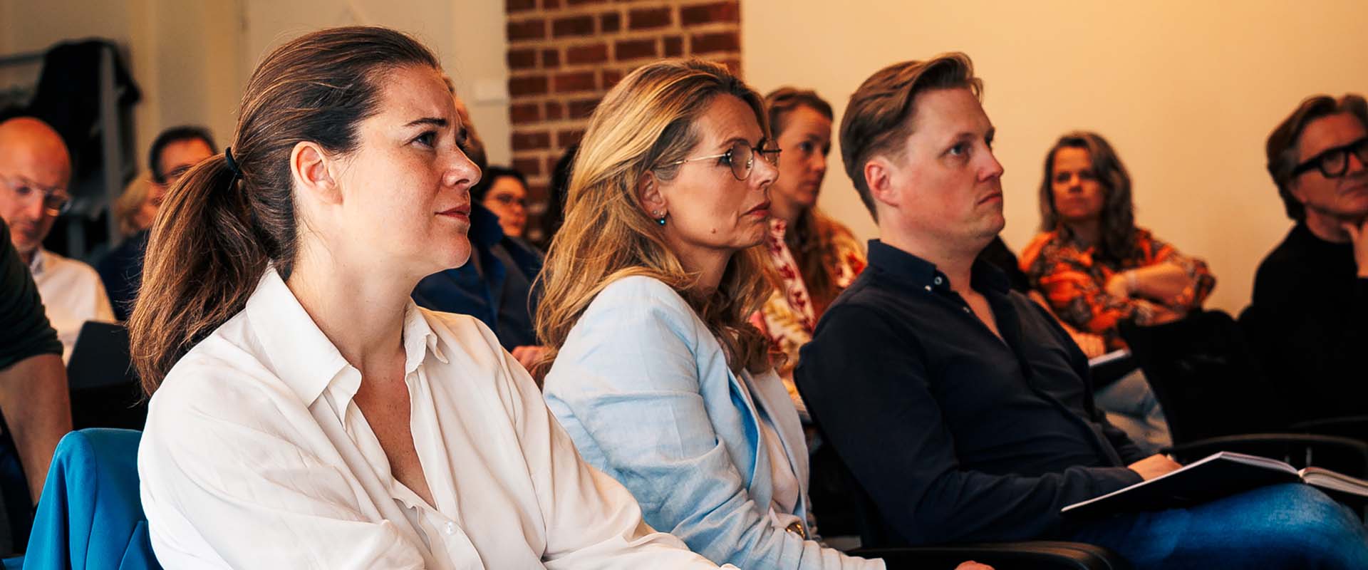 Groep met cursisten zit in grote ruimte en kijkt naar whiteboard